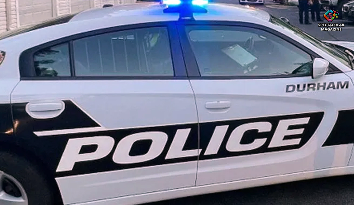 overnight: Side view of a Durham Police Department patrol car with flashing blue lights at night, symbolizing an active investigation.