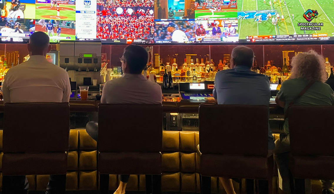 Five people seated at a sports bar betting on multiple live sporting events on large overhead screens