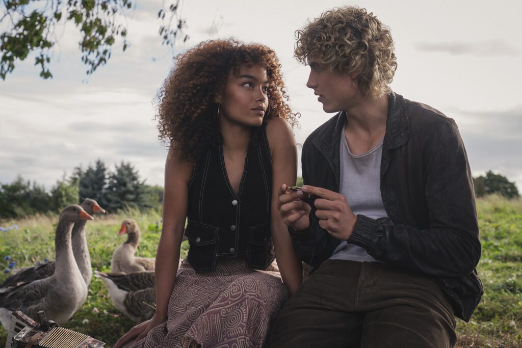Two young characters sit together in a grassy field with several geese nearby in a first-look scene from The Hunger Games: Sunrise on the Reaping.