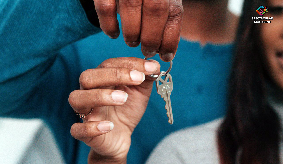 Close-up of a person handing a house key to a woman's outstretched hand, symbolizing the transition from homelessness to stable housing.